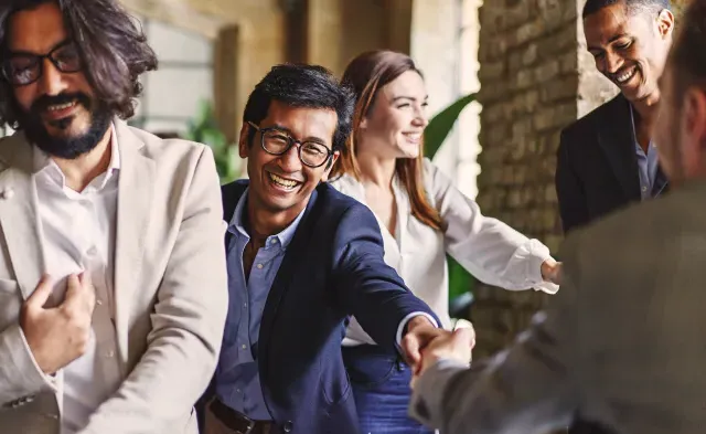 Group of diverse professionals celebrating with a handshake at a corporate event, embodying teamwork and achievement.